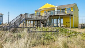 A yellow building with a balcony and a wooden staircase leading to a deck. - Beachfront home with beach access, deck, outdoor shower & washer/dryer (Galveston)