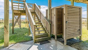 A wooden structure with a staircase leading to a deck area, a small enclosed room, and a view of the beach. - Beachfront home with beach access, deck, outdoor shower & washer/dryer (Galveston)