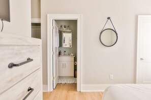 A bedroom with a bed, a dresser, a mirror, and a door leading to a bathroom. - Driftwood Haus - Steps to Beach - 7 Separate Beds - Pet Friendly - Pool - Grill (Gulf Shores)