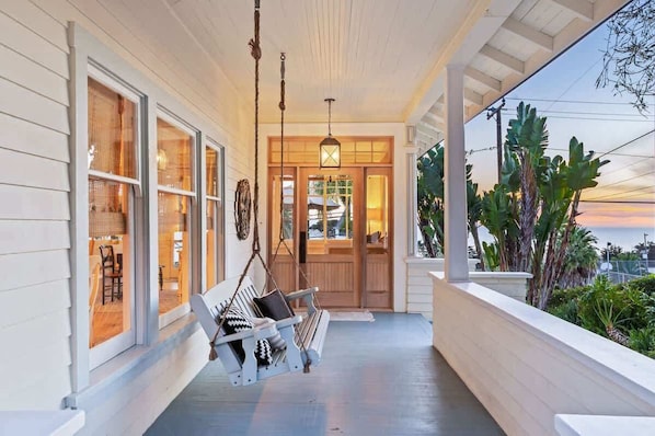 A porch with a swing, a hanging light fixture, and a view of the ocean at sunset.