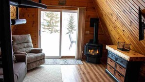 A cozy cabin interior with a sofa, a fireplace, and a sliding glass door leading to a snowy outdoor area. - A-frame, Fireplace,Private Lake Lot, Dock, Kayaks. (Alexandria)
