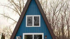 A blue, A-frame house with a sliding glass door and a small patio area with a table and chairs. - A-frame, Fireplace,Private Lake Lot, Dock, Kayaks. (Alexandria)