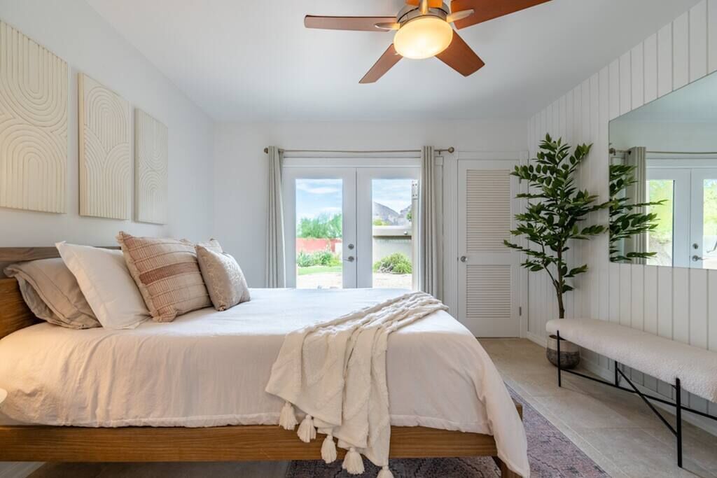 Un dormitorio con cama, ventilador de techo, banco y planta en maceta.