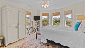 A bedroom with a bed, a wardrobe, a television, and a desk with a chair. - Huge Ocean View Home w/ Elevator, Screened Porch, 2 Primary Suites & 3 Living Areas; Stroll to Beach (Oak Island)