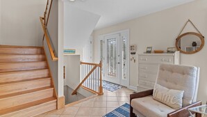 A staircase with wooden steps and a handrail, a white door with glass panels, a chair with a cushion, and a mirror on the wall. - Huge Ocean View Home w/ Elevator, Screened Porch, 2 Primary Suites & 3 Living Areas; Stroll to Beach (Oak Island)