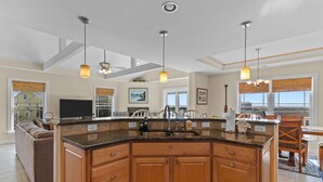 A spacious kitchen with wooden cabinets, a central island, and pendant lighting. - Huge Ocean View Home w/ Elevator, Screened Porch, 2 Primary Suites & 3 Living Areas; Stroll to Beach (Oak Island)