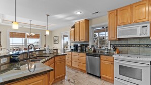 A modern kitchen with wooden cabinets, a granite countertop, stainless steel appliances, and pendant lighting. - Huge Ocean View Home w/ Elevator, Screened Porch, 2 Primary Suites & 3 Living Areas; Stroll to Beach (Oak Island)