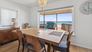 A dining area with a wooden table, chairs, a chandelier, a clock, and a view of the ocean.