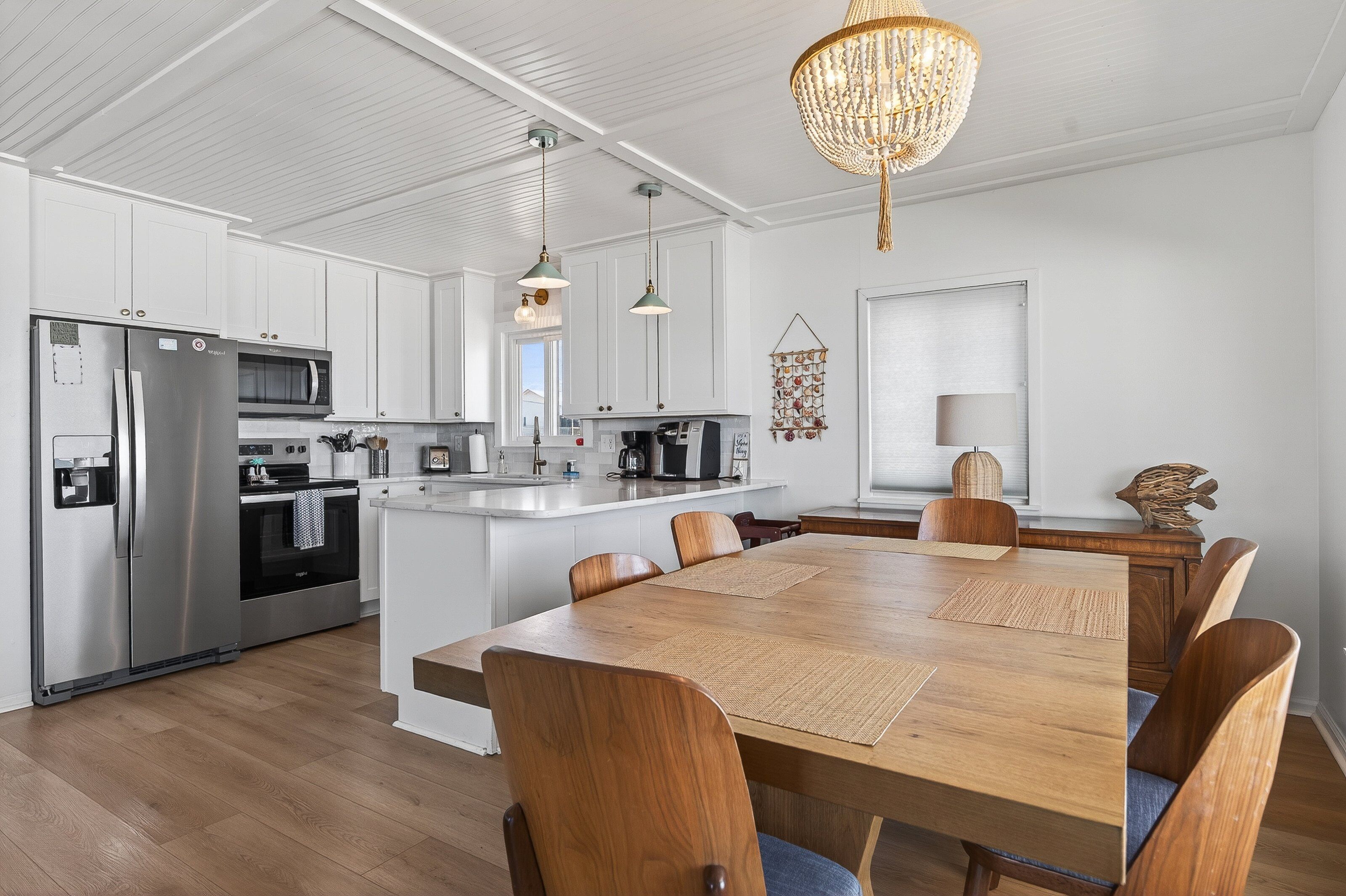 A modern kitchen with white cabinetry, stainless steel appliances, a wooden dining table, and a chandelier.