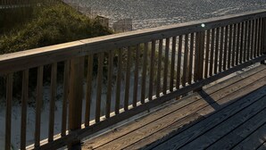 A wooden deck overlooking a beach with the sun setting in the background.