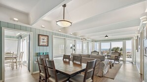 A spacious dining area with a wooden table and chairs, a sofa, and a view of the outdoors. - The Sanctuary -Premier Oceanfront Rental -Large Decks, Pet Friendly! (Folly Beach)
