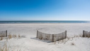 A sandy beach with a wooden fence in the foreground and a clear blue sky. - The Sanctuary -Premier Oceanfront Rental -Large Decks, Pet Friendly! (Folly Beach)