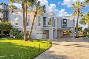 A modern two-story house with a garage, surrounded by a well-maintained lawn and palm trees.