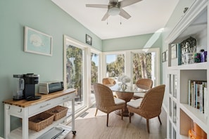 A dining area with wicker chairs, a glass-top table, and a coffee station with a Keurig machine.