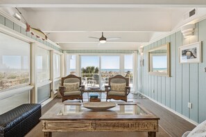 Una habitación luminosa con un ventanal grande, un ventilador de techo y vista al océano.