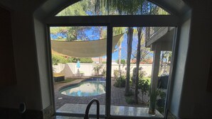 Una cocina con lavamanos y vistas a una piscina en el jardín a través de un ventanal corredero.