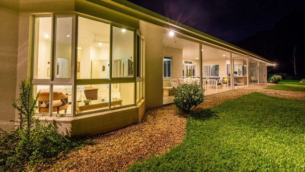 A modern house with large glass windows, a covered patio, and a well-maintained lawn. - Luxury Home in Nature surrounded by Wallabies (Clifton Beach)