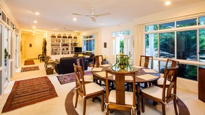 A spacious living room with a round dining table, wooden chairs, a sofa, and a bookshelf. - Luxury Home in Nature surrounded by Wallabies (Clifton Beach)
