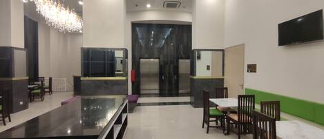 A modern hotel lobby with a marble reception desk, a chandelier, a flat-screen TV, and a green accent wall.