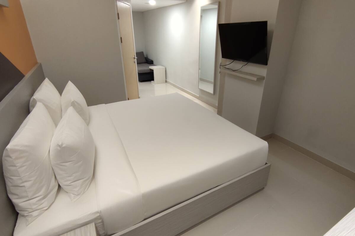 A modern hotel room with a neatly made bed, a flat-screen TV mounted on the wall, and a small bedside table.