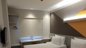 A modern hotel room with two beds, a bedside table, a mirror, a TV, and a bathroom with a sink and towel rack. - Agogo Downtown (Surabaya)