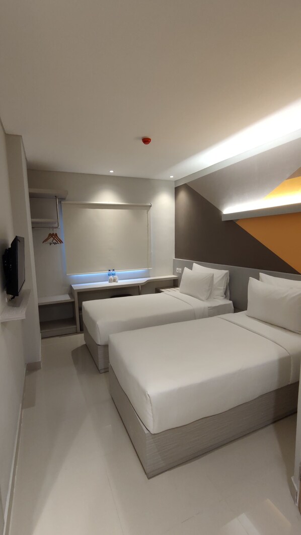 Una habitación de hotel moderna con dos camas, una mesita de noche, un espejo, un televisor y un baño con lavamanos y toallero.
