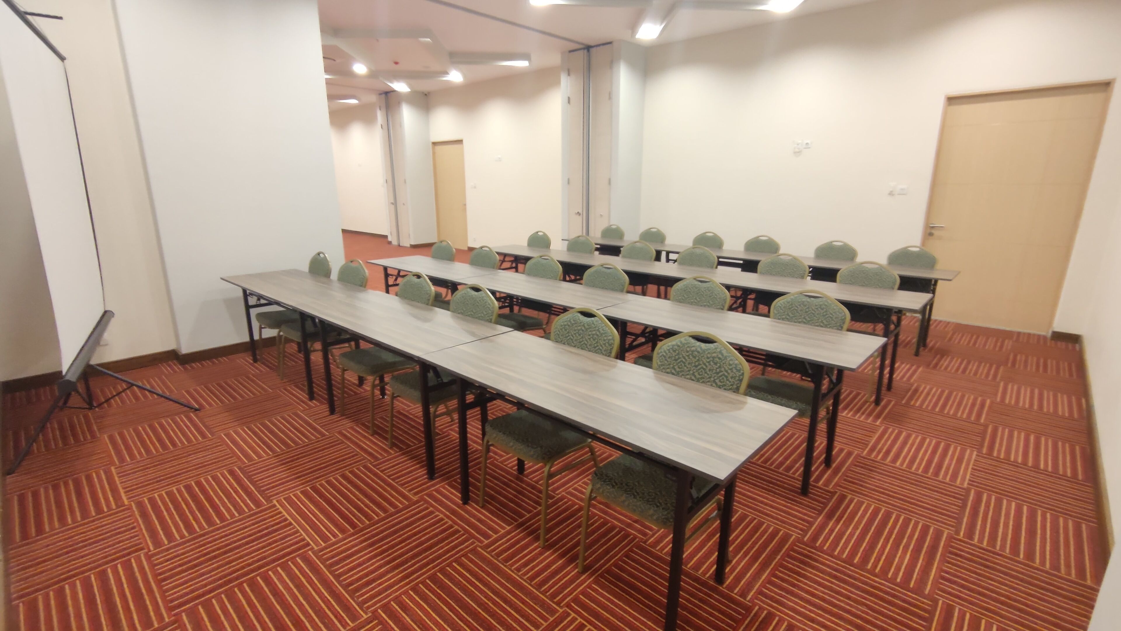 A conference room with multiple tables and chairs, carpeted floor, and a door in the background.