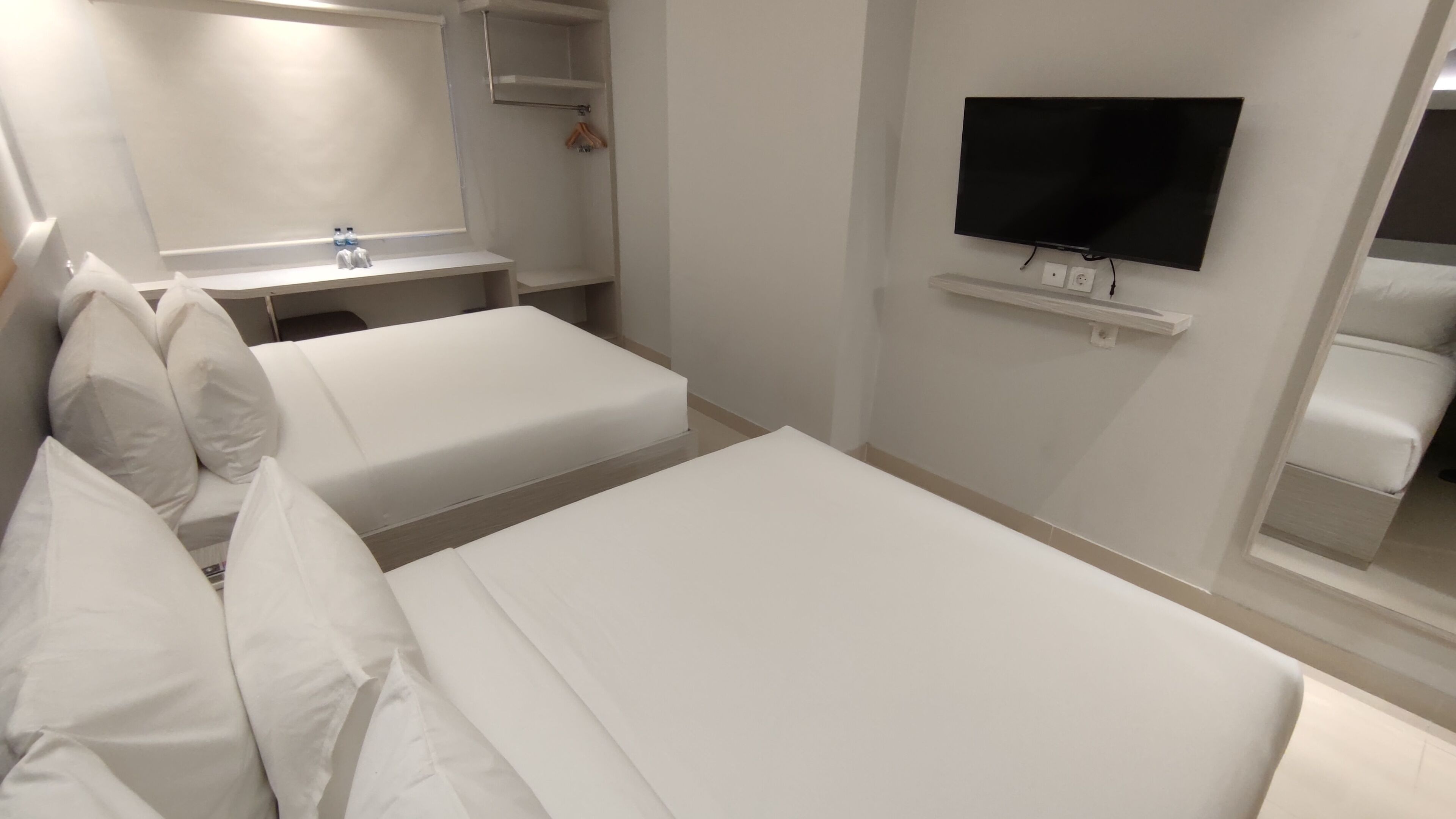 Ein Hotelzimmer mit zwei Betten, einem Fernseher, einem Spiegel und einem kleinen Regal.