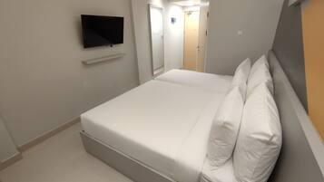 A hotel room with a bed, a television mounted on the wall, and a door leading to a bathroom.