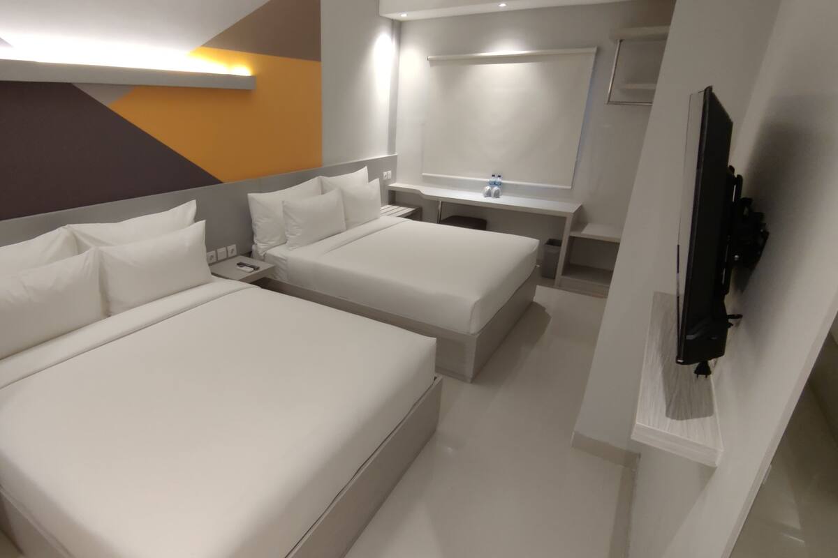 A modern hotel room with two beds, a bedside table, a mirror, a TV, and a bathroom with a sink and mirror.