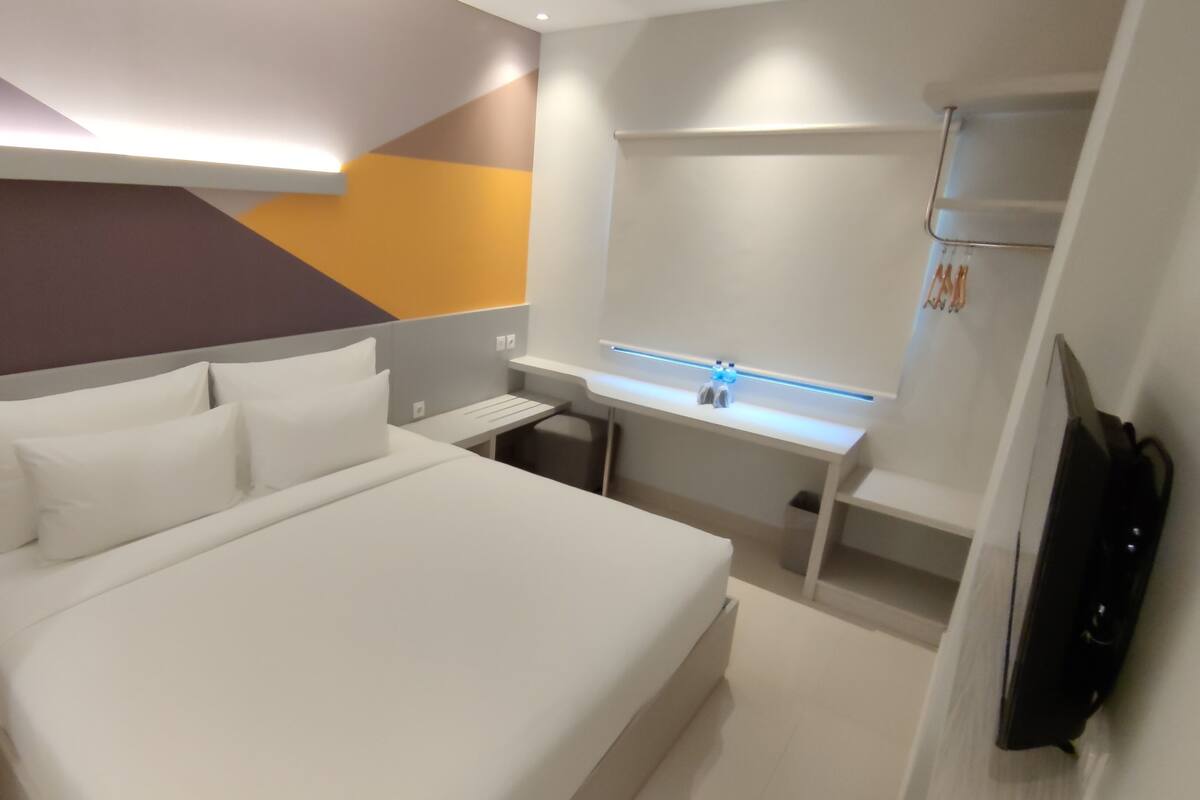 A modern hotel room with a large bed, a desk with a computer, and a bathroom with a mirror and sink.