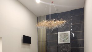 A modern reception area with a marble counter, a hanging chandelier, a mounted television, and a wall-mounted air conditioning unit. - Agogo Downtown (Surabaya)
