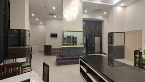 A modern hotel lobby with a marble reception desk, a large chandelier, a television, and a mirrored wall. - Agogo Downtown (Surabaya)