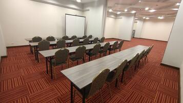 A conference room with multiple tables and chairs, carpeted floor, whiteboard, and a projector screen.