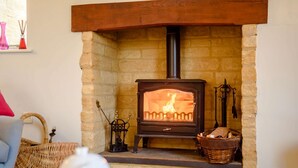 Una chimenea de piedra con estufa de leña, un cesto de leña y una herramienta metálica colgante.