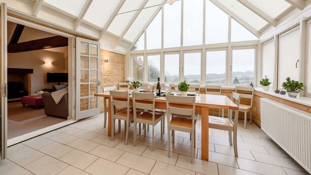Una habitación amplia con techo alto y ventanas grandes, que cuenta con una mesa de comedor y sillas de madera, una chimenea y vistas al campo.
