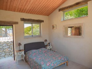 A bedroom with a bed, a nightstand, a lamp, a window, and a stone wall.