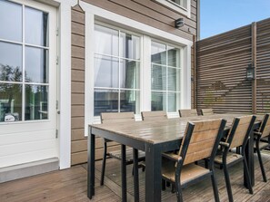 Une terrasse avec une table et des chaises en bois, de grandes fenêtres et une clôture en bois.