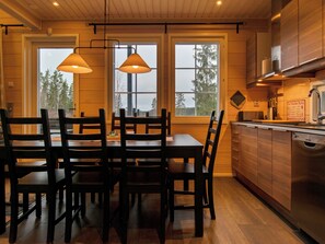 Un interior de madera con mesa y sillas de comedor, ventanas amplias y una zona de cocina.