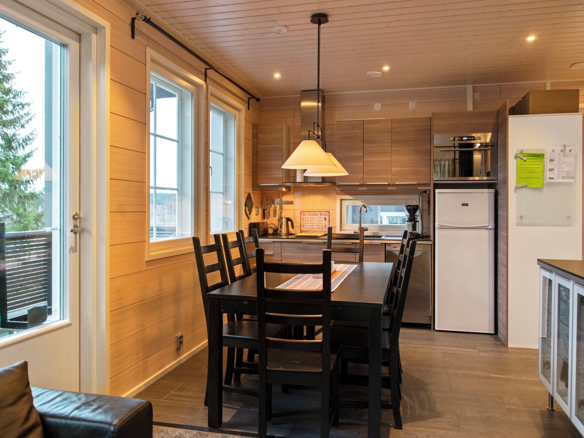 A modern kitchen with wooden paneling, a dining table with chairs, and built-in appliances.