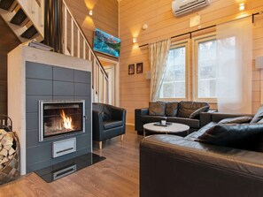 A modern living room with a fireplace, leather sofas, a flat-screen TV, and large windows. - Villa nummenranta 1 by Interhome (Kuhmoinen)