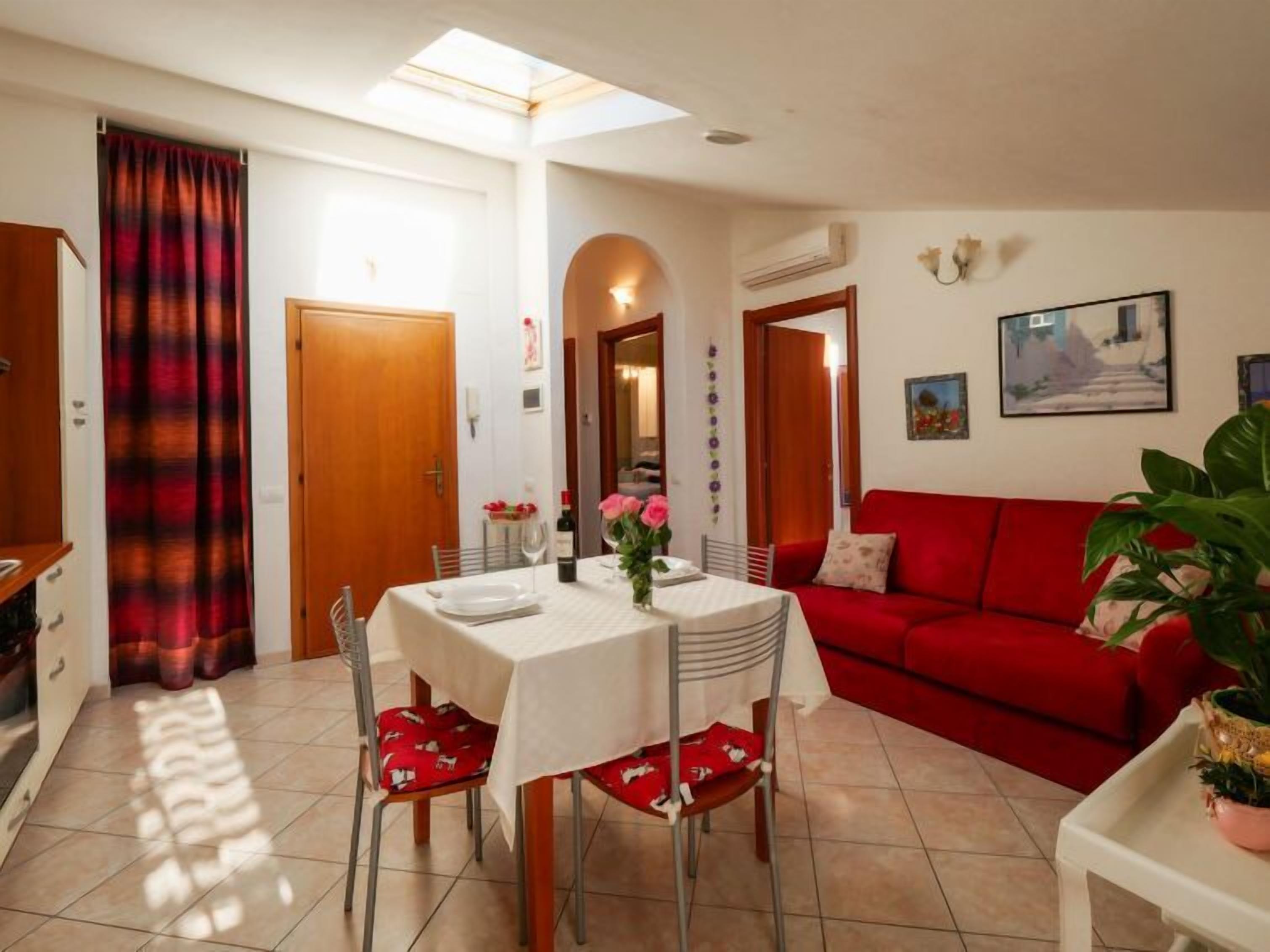 A dining area with a table set for two, a red sofa, and a potted plant.