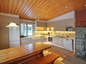 Una cucina moderna con soffitto in legno, mobili bianchi, un tavolo da pranzo in legno e un camino in pietra.