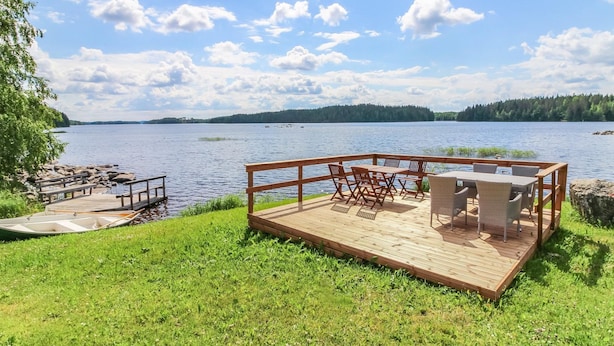 A wooden deck with outdoor furniture overlooking a lake, surrounded by greenery and a clear sky. - Villa lahti by Interhome (Leppävirta)