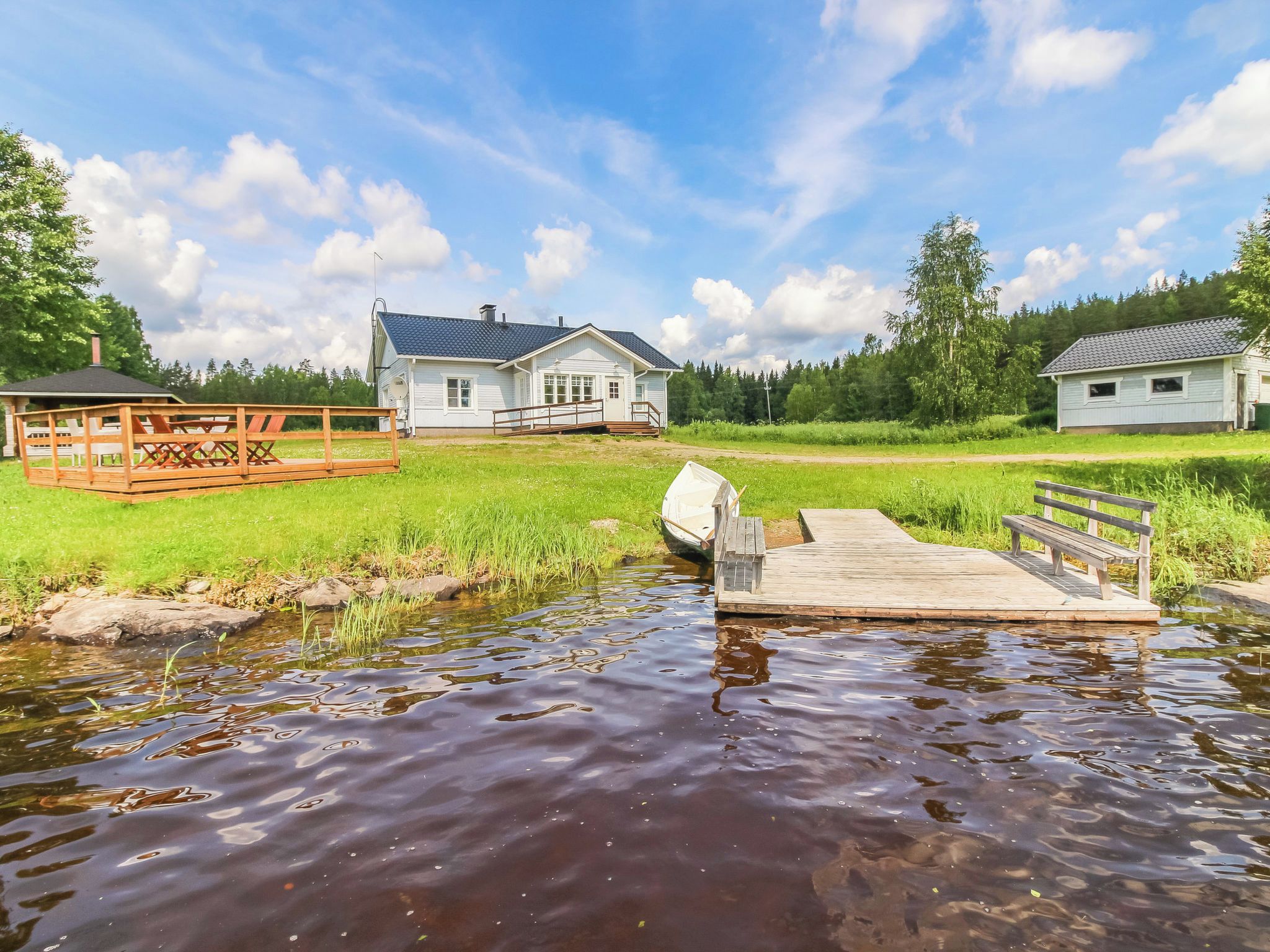 A riverside property with a dock, a small boat, and a house with a blue roof.