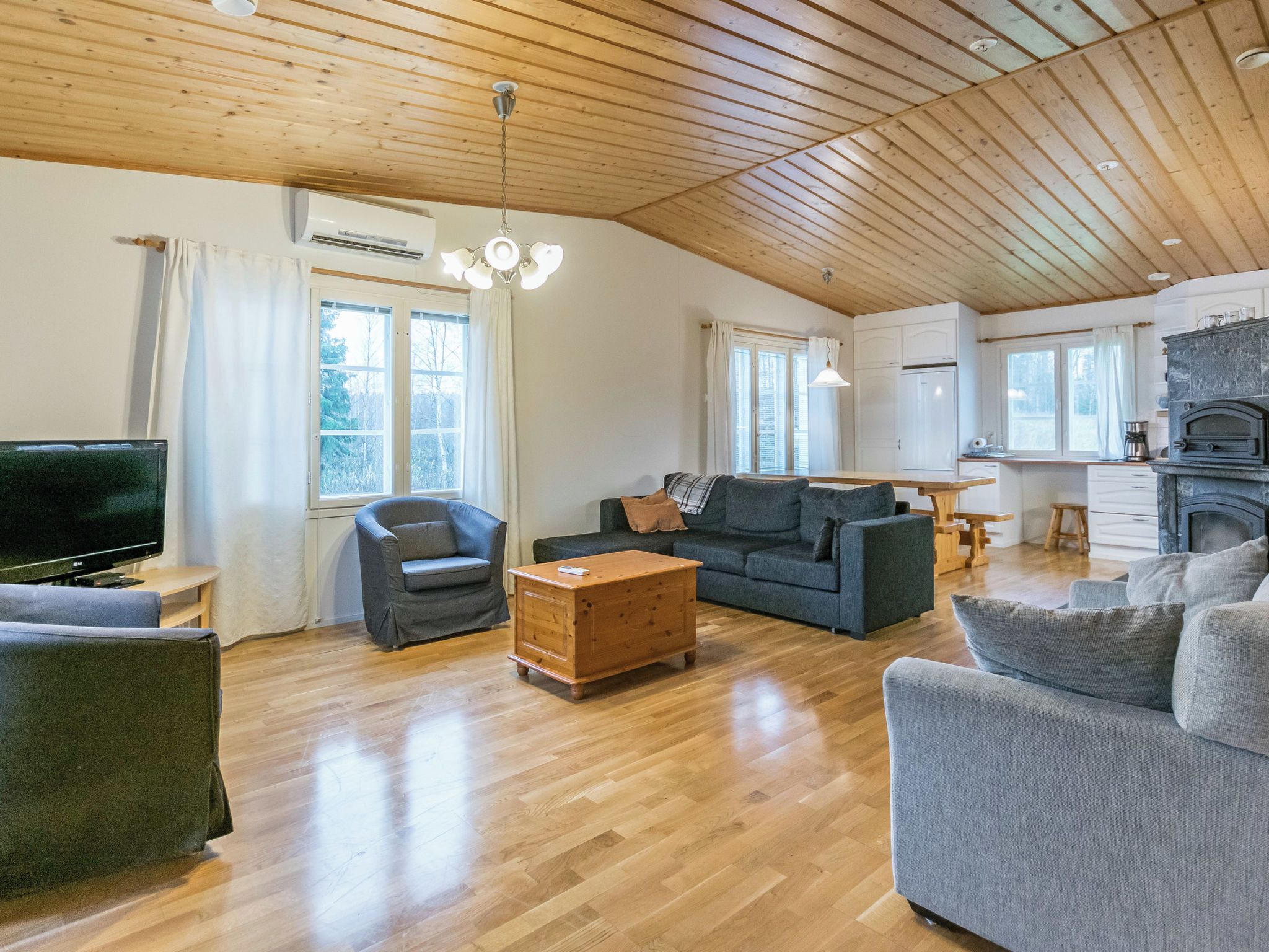 Ein geräumiges Wohnzimmer mit Holzboden, einem Fernseher, einem Sofa, einem Couchtisch und einem Kamin.