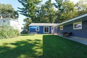 A residential property with a well-maintained lawn, a patio with outdoor seating, and a house with a blue exterior. - Walk to Beach: Lake Michigan Getaway! (Muskegon)