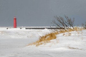 Een rode vuurtoren aan een besneeuwd strand, met een steiger die het water in loopt.