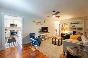 A modern living room with a sofa, armchair, coffee table, and a television. - Walk to Beach: Lake Michigan Getaway! (Muskegon)