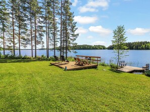 Järvenrantaterassi, jossa on ulkotilaa istumiseen ja näkymä tyynelle, puiden ympäröimälle järvelle.